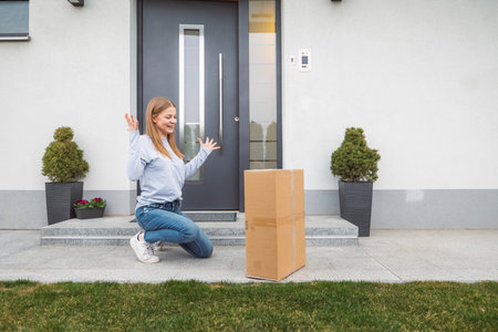 Woman gets overly excited when she sees the cardboard box waiting for her at the front doorの写真素材
