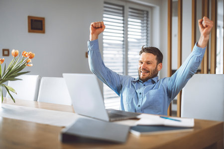 Man watching a football game on laptop, thrilled with his team winningの写真素材