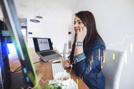 Young caucasian woman working in finance talking on the phone while working on the computer
