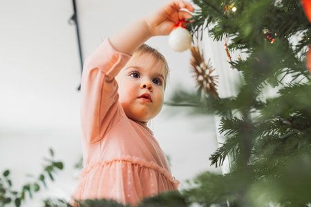 Caucasian baby girl putting Christmas ornament on the tree with focus in her eyesの写真素材