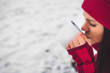 Close up woman drinking tea from a metal cup white in a snowy winter forest on a walkの写真素材
