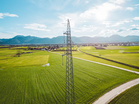 Sun is shining trough the clouds over the electrical tower in the middle of agricultural fields in the country sideの写真素材