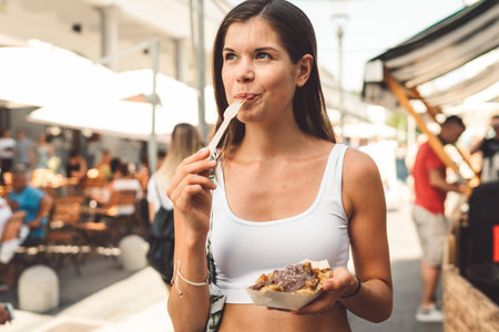 Young woman enjoying her dessert at the food market, licking the fork and smilingの写真素材