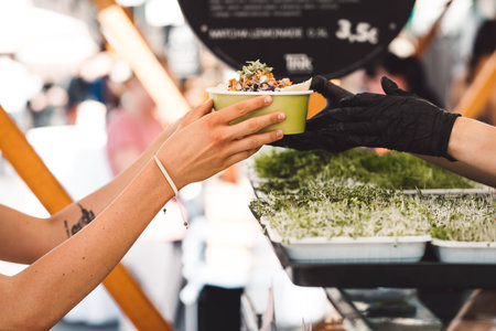 Close up unrecognizable woman hands taking a freshly made poke bowl at a food stand in the city