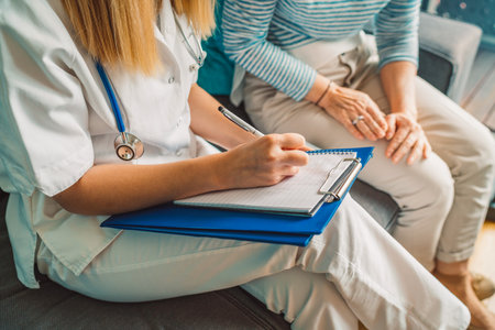 Unrecognizable nurse and senior patient sitting on the sofa, while nurse writes down somethingの写真素材