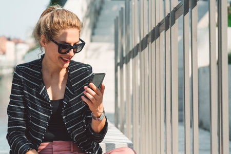 Woman with her hair in a ponytail looking at the phone while on a lunch break outsideの写真素材