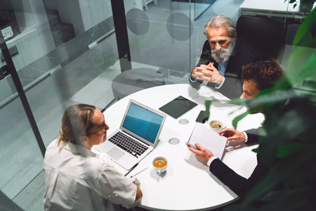 Top down view of three business people sitting by the round table, having a business meeting in a glass officeの写真素材