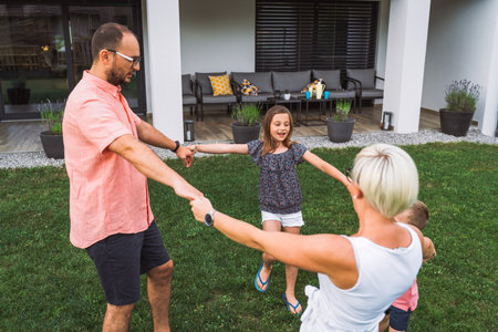 Family holding hands spinning in circle on the grass outside the house