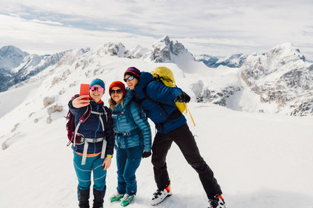 Smiling group of hikers taking a selfie high up in the snowy Alps on a sunny winter dayの写真素材