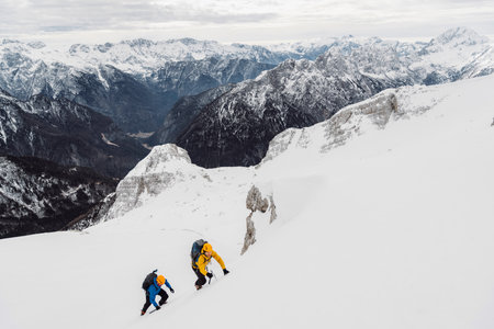 Snowy white Alps and a couple of ski tourers climbing up the mountain to ski back down