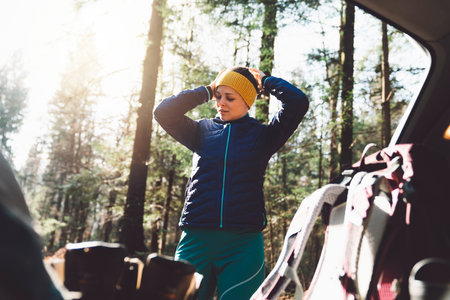 Woman putting on a headband at the trunk of the car, going on a hikeの写真素材