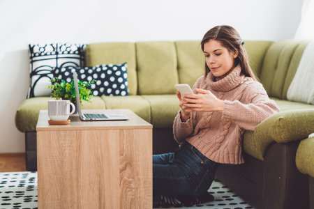 Woman working from home, looking at her phone while sitting on the floorの写真素材