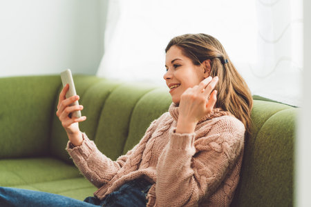 Smiling young woman sitting on the couch on a video call for work, explaining something using her handsの写真素材