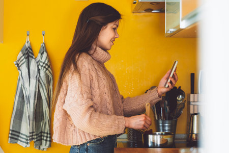 Side view of a woman in her kitchen making lunch while talking on a video call for workの写真素材