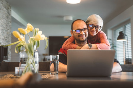 Wife hugging his husband while he works from home on the laptopの写真素材