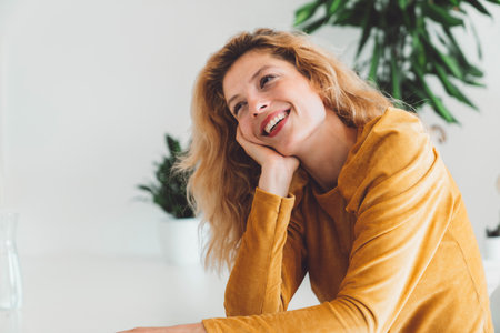 Cheerful smiling caucasian woman portrait, sitting down at the table leaning her head on the palm of her handの写真素材