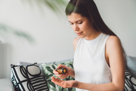 Brunette woman taking her morning vitamins while sitting on the couch at homeの写真素材