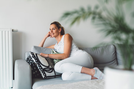 Blonde caucasian woman with a smile on her face, resting on the sofa at home, feeling greatの写真素材