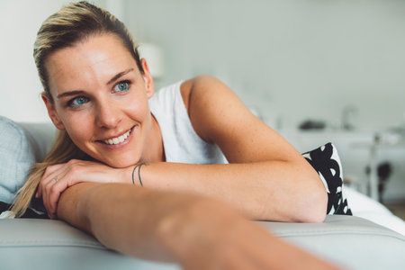 Smiling portrait of a woman with blue eyes laying on the sofa relaxing at homeの写真素材