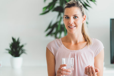 Waist up portrait of smiling blonde woman with blue eyes taking her supplements in the morningの写真素材