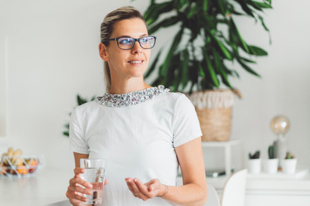Woman with glasses living a healthy lifestyle taking her morning vitamin pillsの写真素材