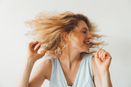 Waist up portrait of cheerful woman playing with her hair, shaking her headの写真素材