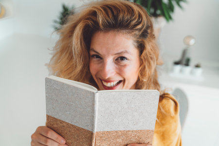 Waist up portrait of a smiling woman hiding behind her notebookの写真素材