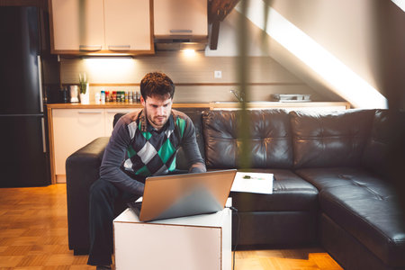 Bearded caucasian man studying on his laptop, online working from his apartment while sitting on the sofaの写真素材