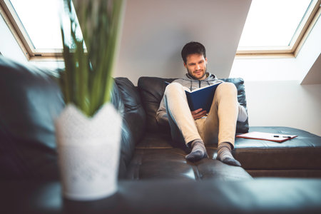 Front view of a man laying on the sofa studying from homeの写真素材