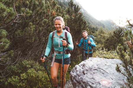 Smiling woman hiker and her partner walking behind her on a beautiful trail up in the Alps early in the morning on a summer dayの写真素材