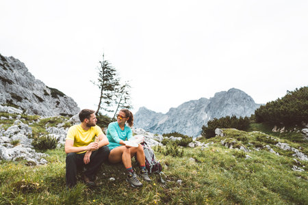 Mountaineering couple sitting down on the grass having a break from hiking a beautiful trail in the summer Alpsの写真素材