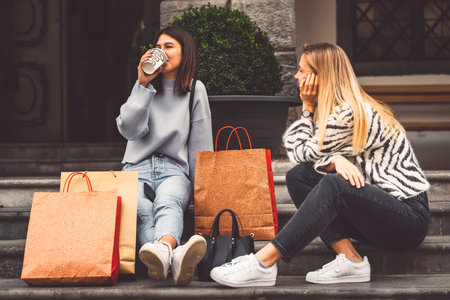 Best friends on a shopping spree at the mall sitting down on the stairs with all the paper shopping bags around themの写真素材