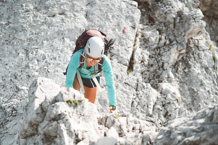 Looking down at woman climber wearing a protective helmet climbing up the mountain on a sunny dayの写真素材