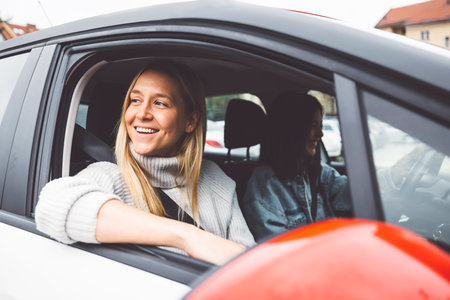 Blonde woman with a big smile on her face sitting in the car looking out the window while parked in the parking lotの写真素材