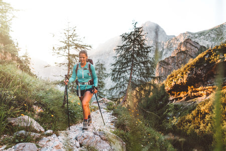 Woman hiker walking with hiking poles on a rocky mountain trail early in the morning on a beautiful summer dayの写真素材