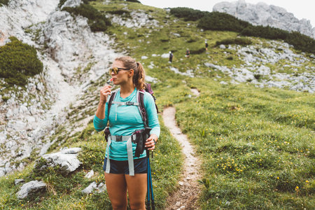 Woman hiker stopping for a moment to drink some water while descending down the mountainの写真素材