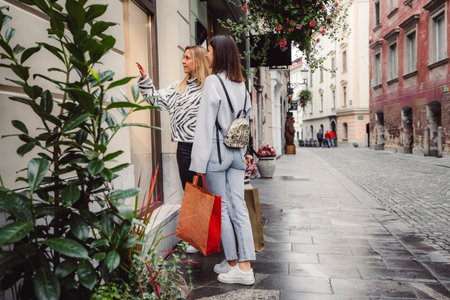 Side view two young women window shopping in the city on a beautiful spring dayの写真素材