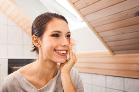 Smiling young woman cleaning her face removing make up with a cotton padの写真素材