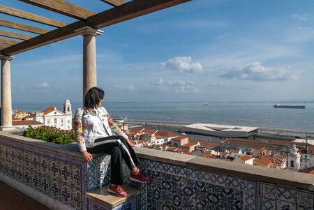 Woman sits on the observation deck and looks at the roofs of the city, the sea, the ship, the sky with clouds on a Sunny dayの写真素材