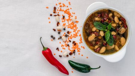 Mexican soup of seven kinds of beans, close-up, on a white linen background surrounded by red and green peppers and beansの写真素材