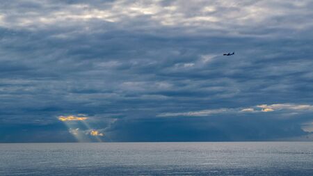The plane flies on the background of clouds over the sea, through the clouds make their way the sun, the French Rivieraの写真素材