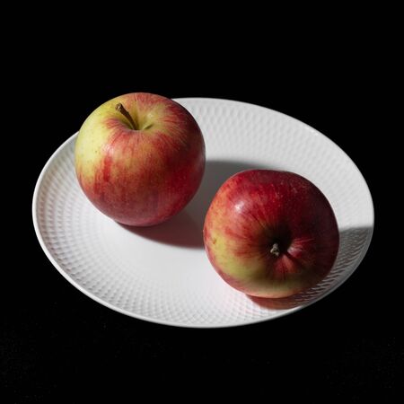 Two apples lie on a white plate on a black background close-upの写真素材