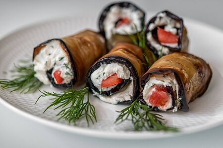 Eggplant rolls with cottage cheese and tomato with dill branches on a white plate close-up on a white backgroundの写真素材