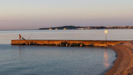 Fishermen catch fish on the pier at sunset. In the background mountains, sky with pink clouds. Franceの写真素材
