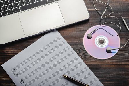 Laptop with headphones, CD and music paper with pen on wooden background. Copy space for your text....