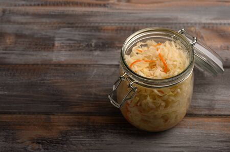 Homemade pickled cabbage with carrots in a glass jar with an open lid on a wooden brown background. Rustic styleの写真素材