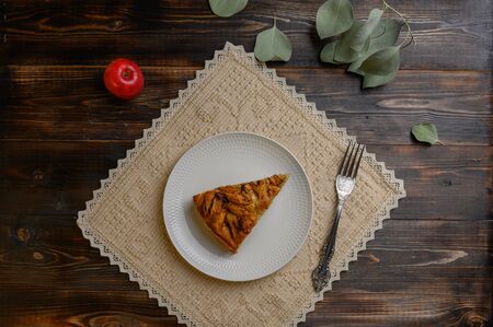 Piece of homemade traditional cornish apple pie on a white plate with a fork on a napkin. Apple and a branch with leaves in the backgroundの写真素材