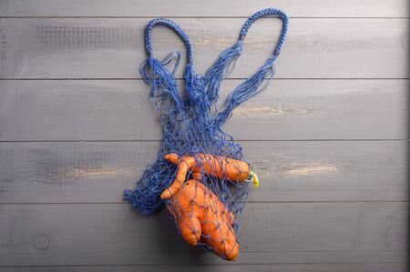 Ugly carrots concept in eco-friendly string bag on wooden background. Copy spaceの写真素材
