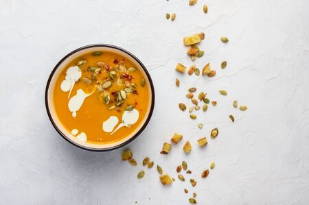 Healthy organic pumpkin cream soup with cream, croutons, seeds and basil on a light wooden backgroundの写真素材