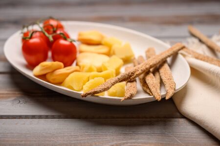 Italian food is grissini bread with prosciutto, cheese and tomatoes with herbs on a plate on a wooden background. Healthy style. Close upの写真素材
